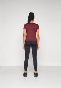 Bordeaux-farbenes Kurzarmoberteil kombiniert mit schwarzen Leggings. Die Leggings haben ein strukturiertes Muster. Beide Teile bestehen aus dehnbarem Material.