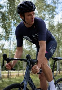 Cyklistický dres, námornícky s bielymi a ružovými akcentmi, s krátkymi rukávmi, priliehavý strih. Cyklista na šedej cestnej bicykli, s čiernou prilbou.