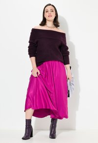 Tumottu tumman violetti neulepusero, joka on yhdistetty vuotavaan fuksiaan maksihameeseen, ja asusteena violetit korot.