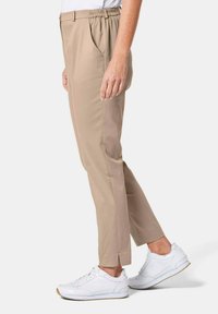 Beige tappered broeken met een elastische tailleband en zijzakken, gecombineerd met witte sneakers. Kenmerkt zich door een cropped zoom met uitsparingen.