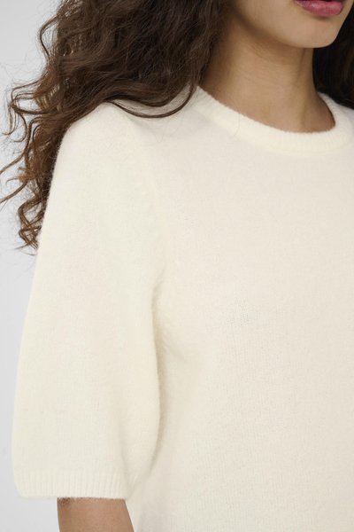 Pull en tricot crème avec des manches courtes légèrement bouffantes et un col rond. Texture douce avec une sensation légère et aérienne.