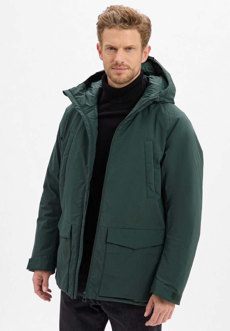 Grüne isolierte Jacke mit Kapuze, ausgestattet mit zwei Fronttaschen, einem durchgängigen Reißverschluss und einer eleganten, glatten Textur. Geeignet für kälteres Wetter.