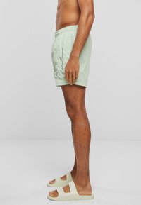 Lysegrønne svømmeshorts med elastisk talje og sidelomme, sammen med lysegule sandaler med udsnitdesign.