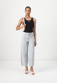 Svart tank topp, lyseblå vide jeans, beige sandaler med logo, liten hvit håndveske, sølvkjede, og flettet hår.