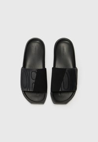 Sorte slide-sandaler med en tekstureret rem, der har hævede bogstaver og en glat mat finish. Flad sål med skrå kanter for stabilitet.