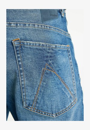 Hintertasche von blauen Jeans aus Denim mit orangefarbenen Nähten und einem Lederlabel mit der Aufschrift "CHASIN'".