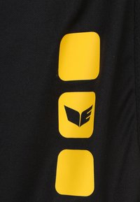 Zwarte stof met een textuur oppervlak, waarop drie gele vierkanten en een gestileerd logo in het geel zijn afgebeeld, met een sterke nadruk op kleur- en ontwerpcontrasten.