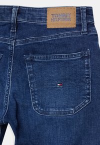 Mörkblå denimjeans med en läderetikett märkta "TOMMY HILFIGER" på midjebandet och en liten logodetalj på bakfickan.