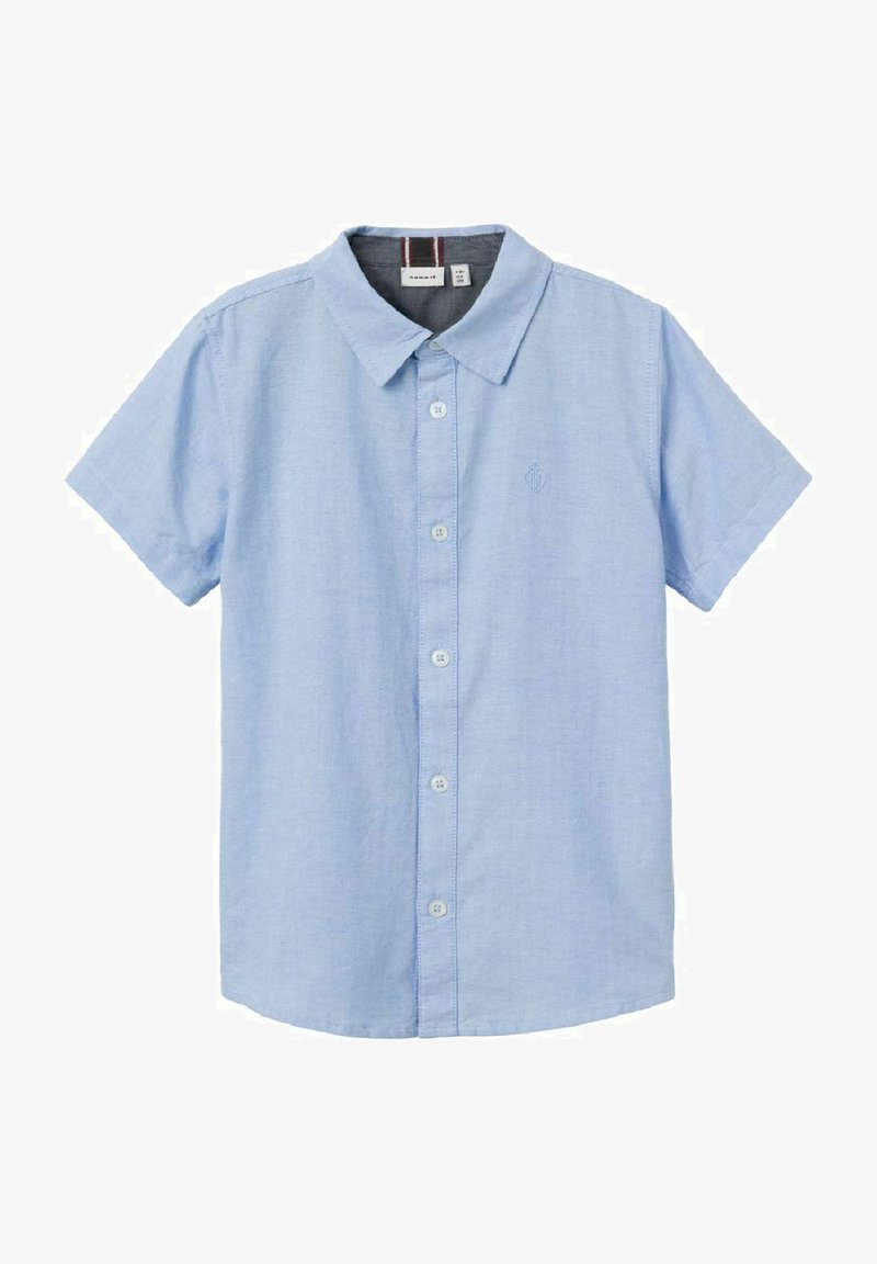 Šviesiai mėlynas trumpo rankovės mygtukų marškiniai, pagaminti iš audinio. Yra apykaklė, iškilūs mygtukai priekyje ir siuvinėtas emblematas krūtinėje.