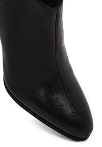 Bota de tobillo de cuero negro con punta afilada y textura suave. Presenta un diseño elegante y un hardware mínimo, que realzan su apariencia aerodinámica.