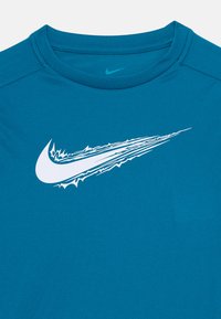 Blå idretts skjorte med en hvit stilisert Nike swoosh-logo som har dynamiske linjer over brystet.