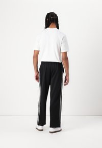 Svart treningsbukser med hvite sidelister, elastisk midje, laget av mykt stoff. Kombinert med en enkel hvit t-skjorte med korte ermer og hvite sneakers.