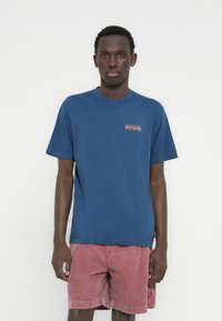 Μπλε βαμβακερό μπλουζάκι με κοντά μανίκια και στρογγυλή λαιμόκοψη, με πολύχρωμο λογότυπο "RIP CURL" στο αριστερό στήθος.