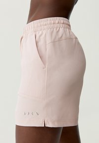 Svetloružové šortky vyrobené z textúrovanej tkaniny, s elastickým pásom, bočnými vreckami a malým logom detailne umiestneným pri leme.