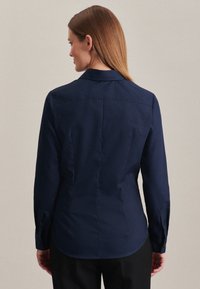 Camicia a maniche lunghe blu navy con colletto a punta, caratterizzata da una texture liscia e cuciture verticali. Polsini con bottone e orlo arrotondato.