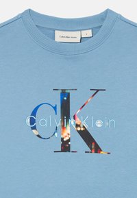 Sweatshirt azzurro chiaro a girocollo con logo "Calvin Klein" caratterizzato da grandi lettere "CK" riempite con un motivo di luci di città.