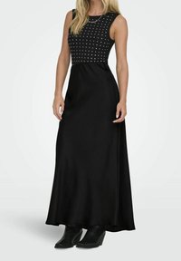 Schwarzes Maxikleid mit ärmellosem Design. Das Oberteil ist mit silbernen Nieten in einem Rautenmuster verziert. Der glatte Stoff weitet sich sanft von der Taille.