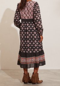 Lång svart klänning med färgglada geometriska mönster, volangkant och broderade detaljer. Kombinerad med bruna ankelboots med fransar.