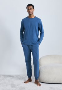 Blå langærmet skjorte og matchende bukser lavet af blødt stof; har elastiske manchetter og et diskret logo på brystet.