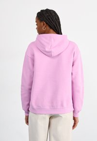 Light pink hoodie with a relaxed fit, hood, and ribbed cuffs. Smooth texture with a kangaroo pocket at the front. Simple design.
