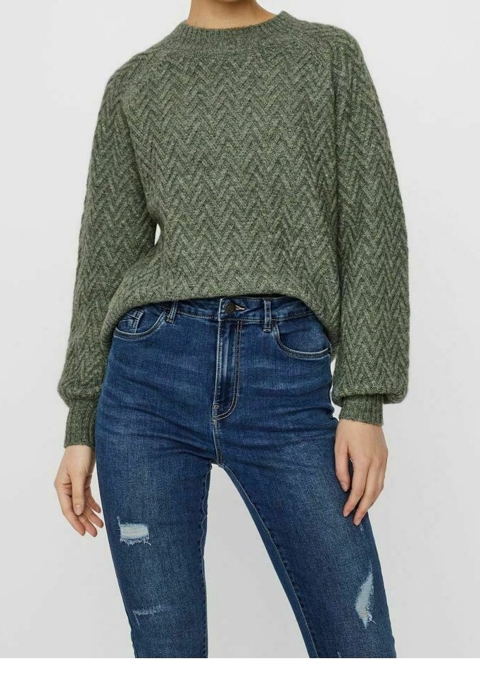 Femme portant un pull en maille texturée vert olive avec des manches bouffantes et un jean skinny bleu déchiré.