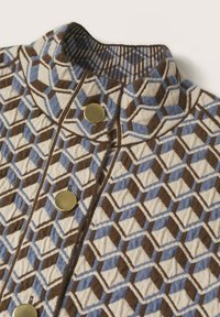 Veste à col montant avec motif géométrique bleu, marron et beige et trois grands boutons ronds dorés à l'avant.