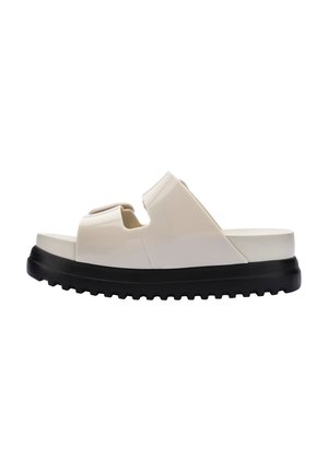 Sandalias tipo slide con un acabado brillante en crema, diseño de punta abierta y una gruesa suela de goma negra con un patrón de textura.