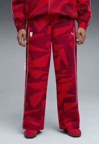 Rode patroon joggingsbroek van lichtgewicht stof, met witte zijstrepen en een logo-patch aan de voorkant, afgewerkt met spitse rode schoenen.