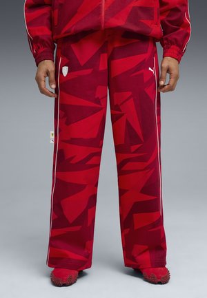 Punaiset kuviolliset treenihousut, jotka on valmistettu kevyestä kankaasta, valkoisilla sivuviivoilla ja etuosassa logopatch. Asusteena piikkikorkoiset punaiset kengät.