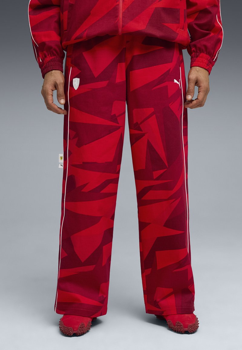 Rode patroon joggingsbroek van lichtgewicht stof, met witte zijstrepen en een logo-patch aan de voorkant, afgewerkt met spitse rode schoenen.