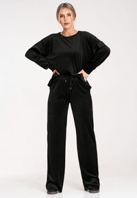 Czarny zestaw wypoczynkowy składający się z luznej, długiej bluzki z długim rękawem oraz spodni dresowych z elastycznym paskiem. Gładka tkanina z sznurkiem ściągającym oraz bocznymi kieszeniami.