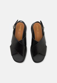 Svarte skinn sandle med slingback, krysset stropper og polstret såle. Har en sølvspenne på siden og en teksturert såle.