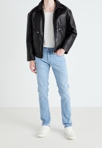 Černá kožená bunda se dvěma předními zipovými kapsami, nošená přes světle šedé tričko, doplněná světle modrými džínami a bílými teniskami.