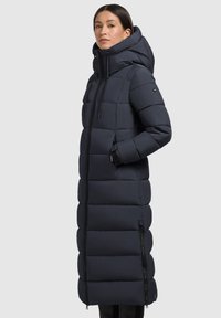 Lungo cappotto imbottito blu navy con collo alto, design trapuntato e vita stretto. Presenta tasche laterali e una zip frontale per la chiusura.