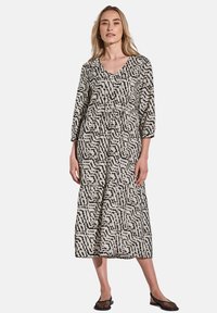 Schwarz-weiß gemustertes Kleid mit V-Ausschnitt, Dreiviertelärmeln, gerafftem Bund und gestuftem Design, aus leichtem Stoff gefertigt.