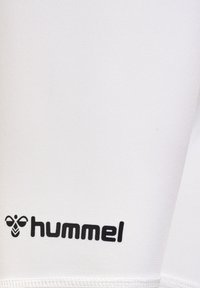 Vita idrottsshorts tillverkade av lättviktig tyg, med en svart "hummel" logotyp nere till vänster och en slät, texturerad finish.