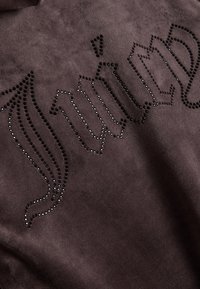 Tissu en daim brun foncé avec de petits clous noirs disposés pour former un texte stylisé de style gothique sur toute la surface.
