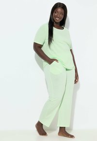 Hellgrünes Lounge-Set bestehend aus einem kurzärmligen Oberteil und langen Hosen, beide aus strukturiertem Stoff mit Taschen an den Hosen.