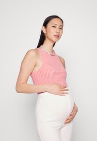 Top sem mangas, em riscas vermelhas e brancas, com um decote redondo, combinado com calças justas de cor clara, realçando a silhueta de uma grávida.