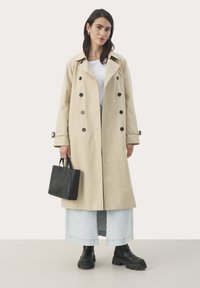Bež trench coat suurte mustade nööpidega, õlavarre epauletid ja vöö. Koos valge särgi, siniste denim-seelikute ja mustade pahkluusaabastega.