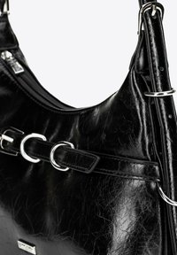 Czarna skórzana torba na ramię o pomarszczonej fakturze, z elementami ze srebrnego metalu, podwójnymi pierścieniami i zamkiem błyskawicznym na górze.
