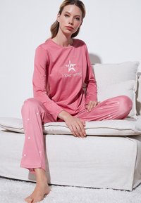 Conjunto de pijama de manga larga rosa con patrón de estrellas blancas, que presenta el texto bordado "Siempre amo el invierno" en la parte superior. Tela suave y ligera.