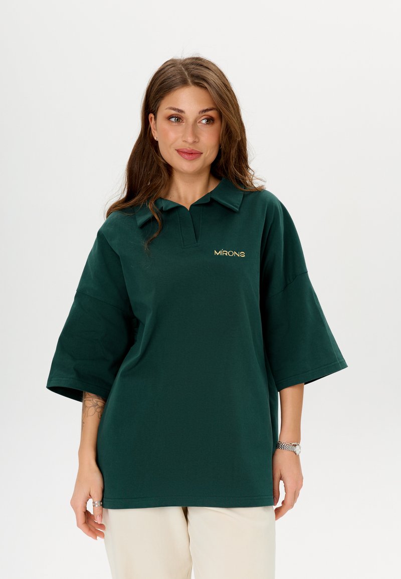 Polo shirt surdimensionné vert foncé à manches courtes, avec un col et un logo doré brodé sur la poitrine. Texture en coton doux.