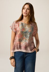 Bloes met een bloemenpatroon in zachte roze en blauwe tinten, gemaakt van doorschijnende stof, met korte, vloeiende mouwen en een gebogen zoom. Draag het met losse denim jeans.