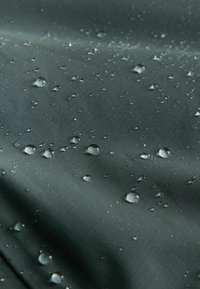 Waterproof fabric in dark green with textured surface, featuring droplets of water. Consistent pattern with visible sheen from moisture.