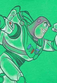 Grünes T-Shirt mit einem Aufdruck eines Cartoon-Charakters in einem Raumanzug, mit grauen und blauen Akzenten, umrandet von Schwarz.