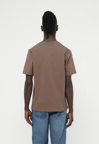 Κ αφέ βαμβακερό t-shirt με κοντά μανίκια και στρογγυλή λαιμόκοψη, με άνετη εφαρμογή. Η πίσω όψη παρουσιάζει μια λεία επιφάνεια και ελάχιστες λεπτομέρειες.