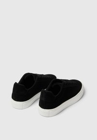 Le sneakers in suede nero presentano una punta rotonda, una suola piatta in gomma bianca e un design con lacci. La parte posteriore ha un leggero accento sul tacco.