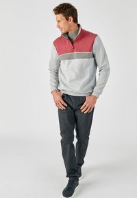 Sudadera gris con rayas horizontales rojas y grises, cuello con cremallera y mangas largas; combinada con jeans oscuros y zapatillas oscuras.
