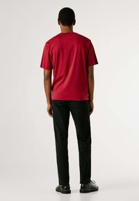 Camiseta de algodón roja con mangas cortas, cuello redondo y corte holgado, combinada con pantalones negros y zapatos negros con cordones.